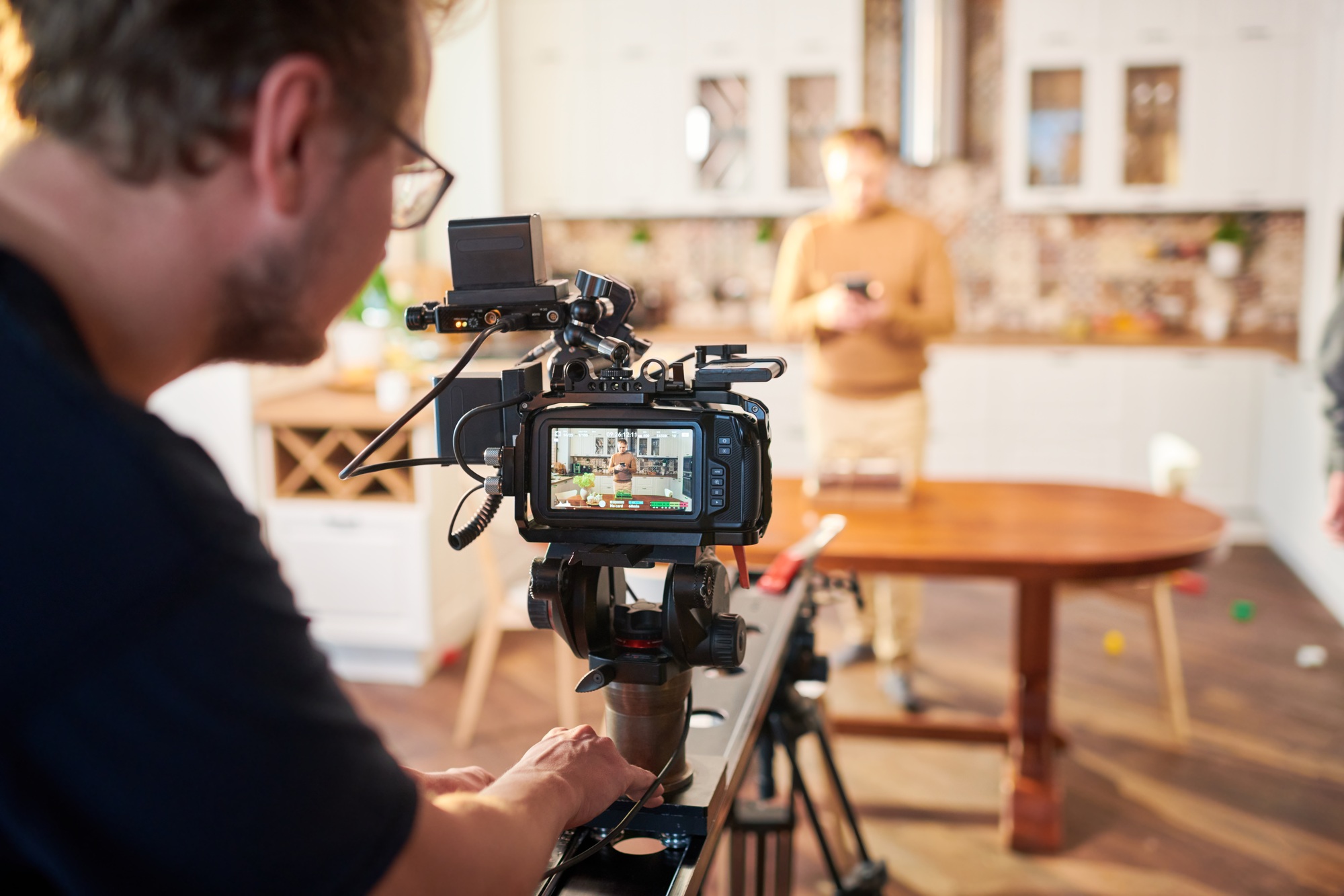 Young male videographer standing by video camera while shooting advertisement Young male videographer standing by video camera while shooting advertisement